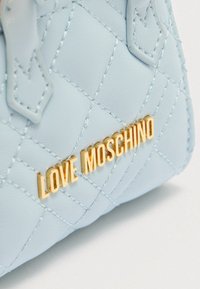 Τσαντάκι ώμου σε ανοιχτό μπλε χρώμα, κατασκευασμένο από συνθετικό δέρμα, με χρυσό λογότυπο "LOVE MOSCHINO" και αντίθετες ραφές.