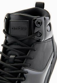 Vysoké černé tenisky s koženými a lakovanými akcenty, s texturovaným povrchem, plochými tkaničkami a gumovým štítkem s logem.