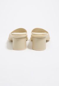Beige open-toe block hak sandalen met gevoerde zolen, van achteren getoond op een witte achtergrond.