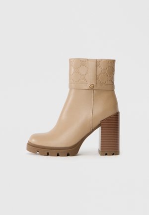 Bottes cavalières beiges en matériau lisse, avec une tige texturée ornée de motifs en relief, un talon en bois épais et une semelle en caoutchouc.