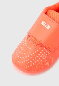 Πορτοκαλί ελαφρύ παπούτσι με ανάγλυφο επάνω μέρος που διαθέτει λευκό διακοσμητικό σχέδιο, στερεωμένο με λουράκι βέλκρο. Κοντινή λήψη.