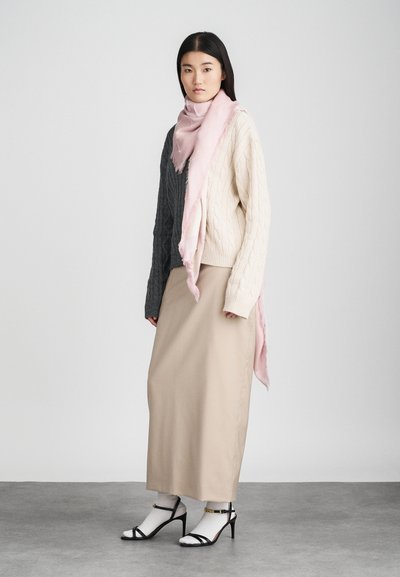 Cachecol rosa claro colocado sobre um suéter de malha em creme e cinza, combinado com uma saia longa bege e sapatos de salto abertos pretos com tiras.