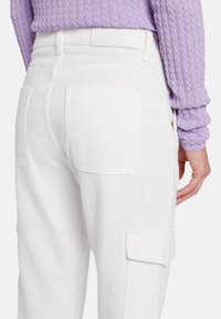 Pantaloni cargo in denim bianco con tasche laterali, caratterizzati da una texture liscia e linee pulite. La vita è semplice, senza hardware visibile.
