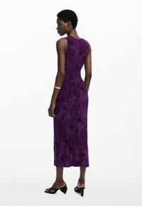 Robe sans manches violette avec un motif floral et une surface texturée. Longueur au-dessous du genou avec une silhouette ajustée. Sandales à talons noires.