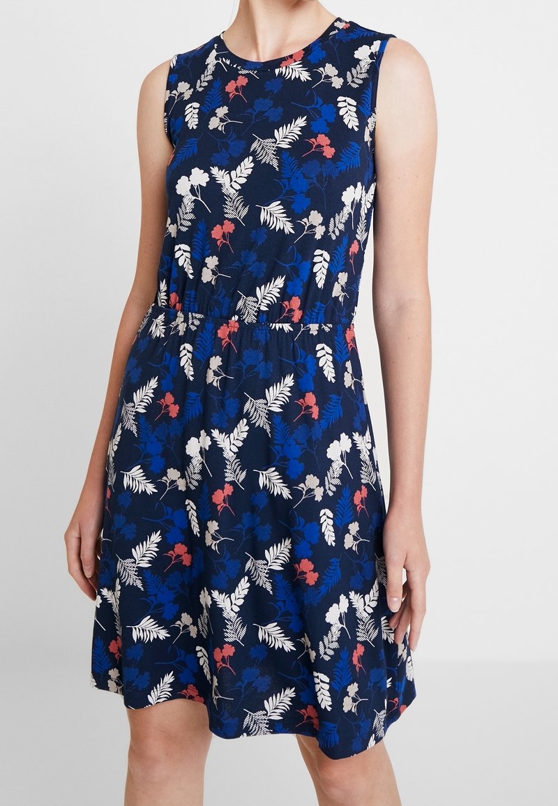 Robe fleurie bleu marine avec un design sans manches, une taille froncée et des motifs de fleurs blanches, rouges et bleues sur un tissu doux.