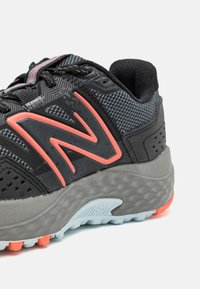 Zapatilla de correr negra con una parte superior texturizada, acentos naranjas y una suela gris con un diseño estampado y detalles de amortiguación.