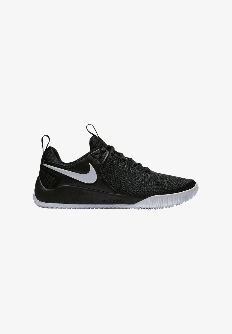 Sort atletisk sko med en tekstureret overdel, mesh-paneler og et hvidt swoosh-logo. Har en robust sål og trækkapsler ved hælen.