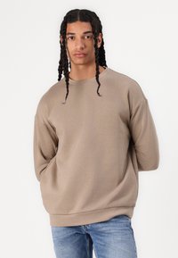 Bruine oversized sweatshirt met een ronde hals, lange mouwen en ribbelzoom, gecombineerd met lichtblauwe jeans. Soepele textuur, casual pasvorm.