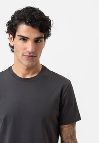 Donkergrijze, aangesloten T-shirt met een ronde halslijn en korte mouwen. Glad textuur met minimale details en geen zichtbare patronen.