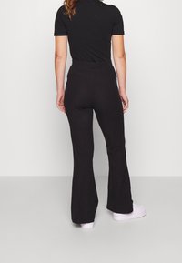 Svarta utsvängda byxor med hög midja, tillverkade av textil med struktur. Kombineras med en figursydd svart kortärmad topp och vita sneakers.