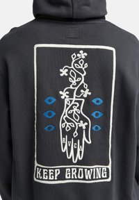 Black hoodie featuring a white embroidered design of a hand with vines, blue eyes, and the text "KEEP GROWING" in white. Soft texture.