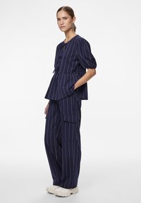 Námořnický pruhovaný outfit skládající se z peplum topu s balónovými rukávy a vysokými kalhotami s kapsami, doplněný světle barevnými teniskami.