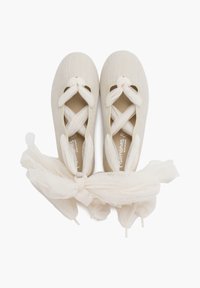Light beige ballet flats with crossed lace ties and tulle ribbons, positioned side by side on a plain background.