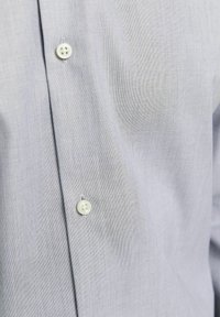 Camicia azzurra chiara con un delicato motivo a trama, dotata di un bottone in plastica bianco e di un classico design del colletto.