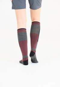 Knähöga strumpor med maroon, grå och svarta ränder; stickat tyg med ribbad topp. Designade för komfort och hållbarhet.