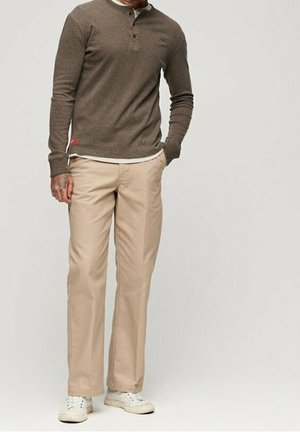 Brun henley-skjorte med lange ærmer og tre-knaps plaket, stylet med lyse beige bukser med lige ben og hvide sneakers.