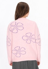 Różowy sweter dzianinowy z dużymi fioletowymi wzorami kwiatowymi, ściągacze przy mankietach oraz perełki ozdabiające rękaw. Teksturowany, luźny fason.