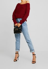 Maglione rosso a coste, design scollato, abbinato a jeans azzurri con risvolto. Borsa nera con una superficie texturizzata e dettagli in metallo argentato.