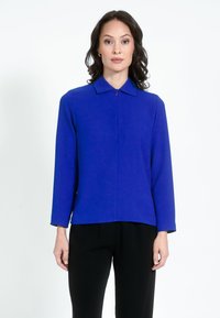 Kék, hosszú ujjú blúz gallérral, elülső cipzárral és sima szövettextúrával, fekete nadrággal párosítva.