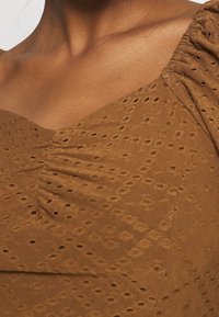Brun klänning med ett texturerat mönster, med en hjärtformad ringning och samlad detalj vid axlarna, tillverkad i ett lätt material.