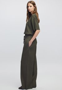 Dvojdílný outfit v olivově zelené barvě, který obsahuje volný krátký rukáv top a kalhoty širokého střihu se bočními kapsami a elastickým pasem se stahovací šňůrkou.