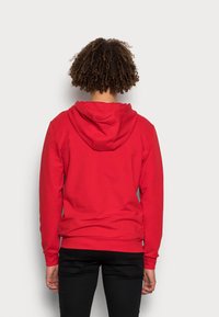 Felpa rossa con cappuccio, maniche lunghe e tasca a marsupio. Realizzata in tessuto misto cotone, con polsini e orlo a coste.