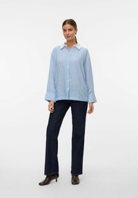 Blå och vit randig oversized skjorta med vit krage och långa ärmar, tillsammans med mörkblå raka jeans och bruna ankelstövlar.