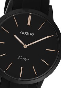 Montre analogique noire avec une finition mate lisse, des index et aiguilles en or rose. Présente le nom de la marque "OOZOO" et "Vintage" en texte blanc.