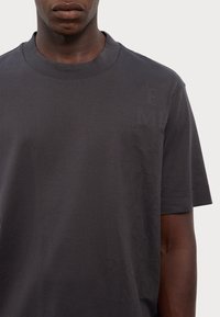 Gray cotton T-shirt with a crew neckline and short sleeves. Features embossed text patterns on the front. Soft texture, minimalistic design.