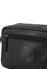Černá kožená taška s kapsou na zip, s embosovaným logem, hladkým povrchem, obdélníkovým tvarem a kontrastními zlatými akcenty.