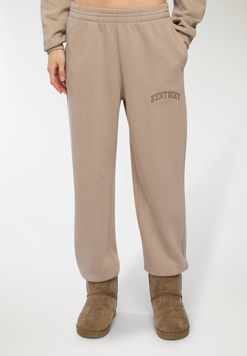 Pantaloni della tuta beige con design a gamba dritta, caratterizzati da un ricamo con la scritta "KENTUCKY". Tessuto in cotone morbido con fascia elasticizzata in vita.