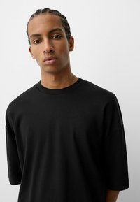 Tricou negru oversized cu guler rotund și mâneci scurte, fabricat dintr-un material neted, cu un croi lejer și fără modele vizibile.