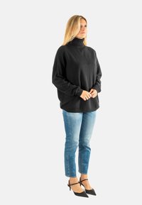 Zwarte oversized trui met een hoge kraag, gecombineerd met lichtblauwe denim jeans en zwarte puntige hakken. Soepele stof en een relaxed fit.