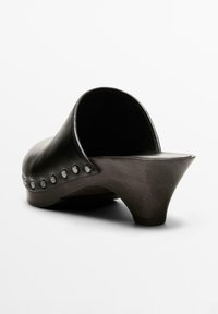 Svarta läderklackar med böjd häl, med metallnitar längs sidan och en slät konturerad form.