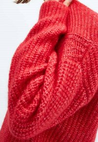 Pull en tricot rouge présentant un motif texturé, une coupe ample et de larges poignets côtelés. Le matériau semble doux et légèrement épais.