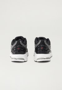 Des chaussures de sport noires et grises avec une tige en mesh, un col rembourré et une semelle blanche avec des accents gris et un logo sur le talon.