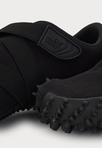 Gros plan de baskets noires Puma avec semelles texturées et design à brides croisées affichant le logo de la marque sur le côté.