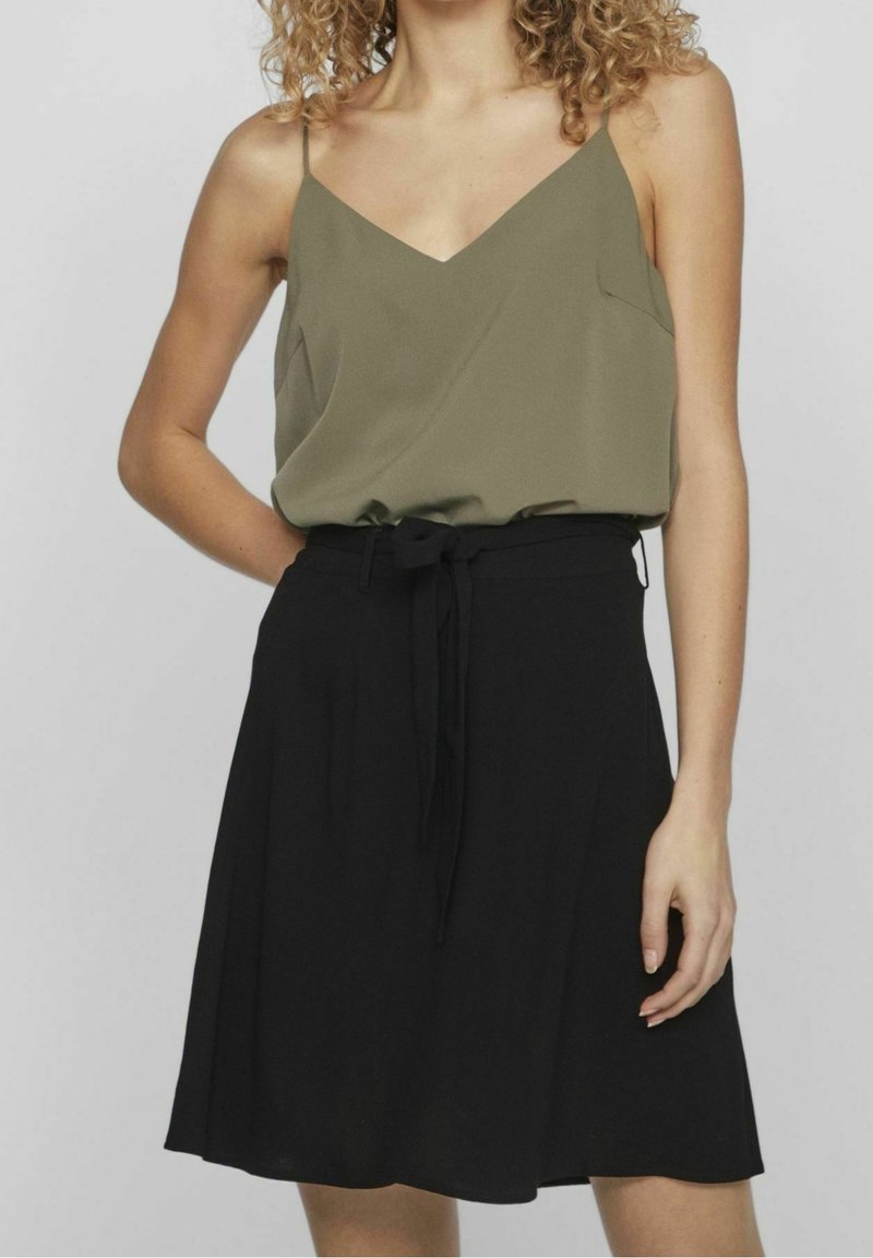 Ärmlös olivgrön topp med V-ringning, i kombination med en svart kjol som knyts i midjan. Mjuk tygkvalitet med en flödande siluett och avslappnad design.