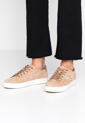 Beige semišové tenisky s bílou gumovou podešví, kulatou špičkou, šněrováním na přední straně a kovovými akcenty na patě. Texturovaný povrch a prošívané detaily.