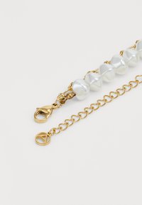 Gold chain bracelet featuring six glossy white pearls, with a lobster clasp and a circular charm embossed with a letter "A."
