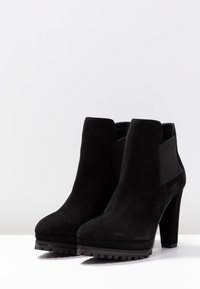 Černé nubukové kotníkové boty na vysokém podpatku, s hladkým povrchem a elastickými bočními panely. Robustní podrážka pro lepší p�řilnavost.