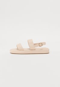 Nude sandals with two wide top straps and an adjustable ankle strap. Flat sole with a slight texture. Buckle detail on the ankle strap.