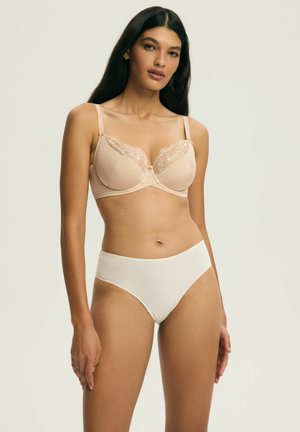 Beżowy biustonosz z koronkowym zdobieniem na miseczkach i regulowanymi ramiączkami, w komplecie z białymi majtkami z wysokim stanem, gładka tekstura tkaniny.
