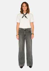 Jean gris à jambes larges, taille haute, poches avant, assorti à un t-shirt blanc à col rond et un bandana noir. Texture denim lisse, design décontracté.