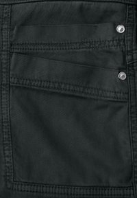 Kieszeń z ciemnozielonego materiału z dwoma metalowymi nitami na górnych prawych rogach oraz widocznymi detalami przeszyć.