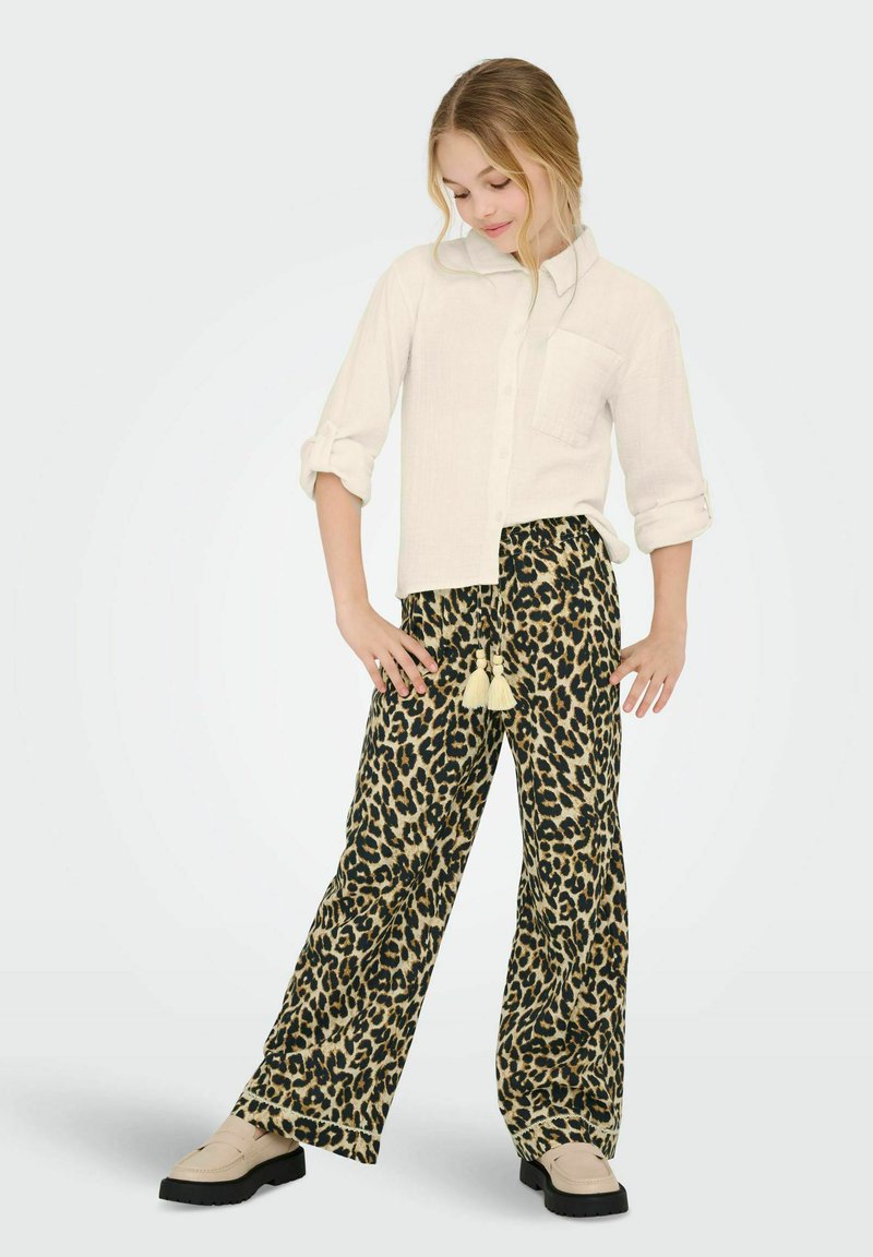 Bílá dlouhá košile s knoflíky, s vyhrnutými rukávy a náprsní kapsou, doplněná širokými kalhotami s leopardím vzorem a zavazováním na třásně.