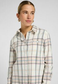 Kraagloos flanellen shirt in roomkleur met een meerkleurig ruitpatroon. Voorzien van knopen, een borstzak en een klein logo vlakbij de zak.