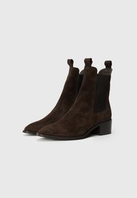 Bottines en suède marron avec un bout pointu et des panneaux latéraux élastiques. Elles sont dotées de petites languettes de tirage et d'un talon bas épais.