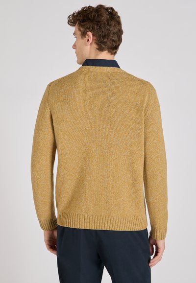 Pull en maille jaune moutarde avec une finition texturée, des poignets côtelés et un col rond. Porté par-dessus une chemise à col bleu marine, sans motifs visibles.