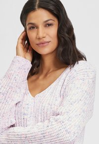 Helles rosa, gestricktes Sweatshirt mit V-Ausschnitt-Design, das ein strukturiertes Muster und subtile blaue und lila Sprenkel aufweist.